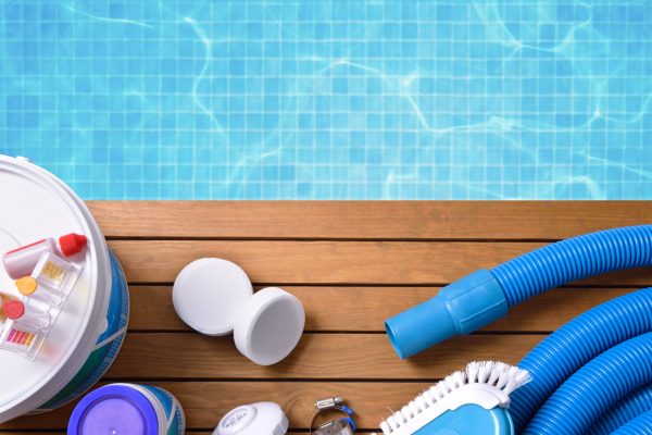 Chemical products and tools for the maintenance of the pool on wooden slats. Pool with water and blue mosaics background. Horizontal composition. Top view